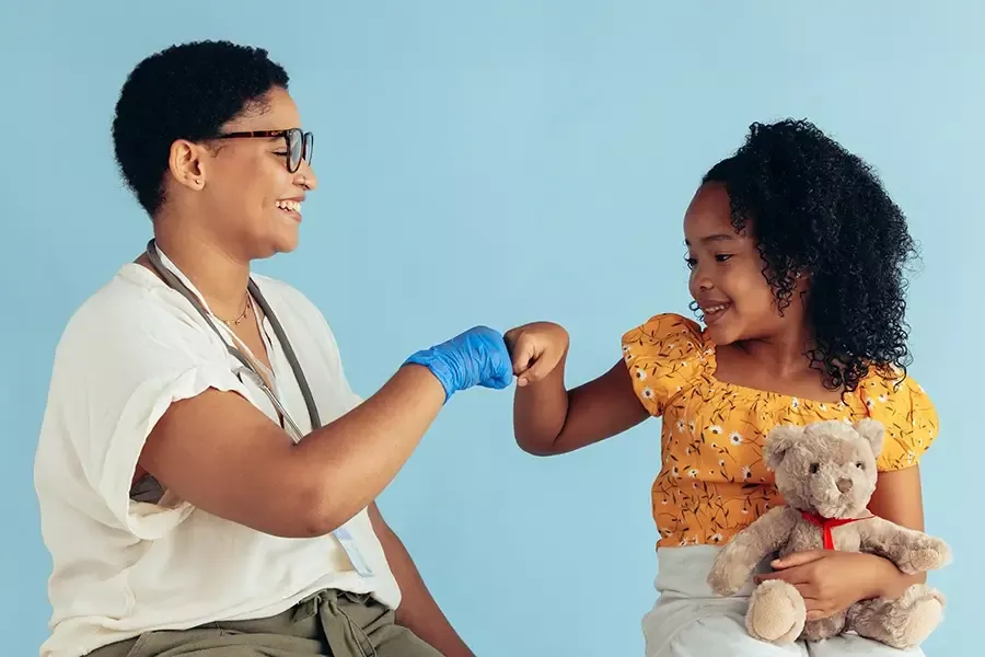 Medical person fist bumping with little girl patient holding a teddy bear