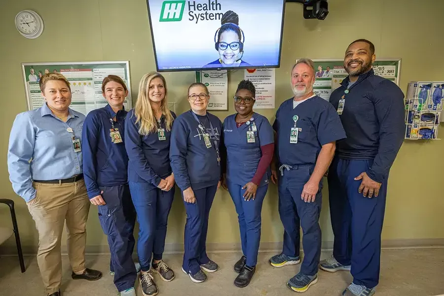Huntsville Hospital team members pose for a photo with the virtual care nurse on the screen above them.