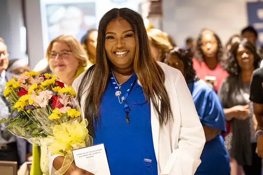 A graduate of the inaugural class of the LPN Launch program is holding a bouquet of flowers and smiling.