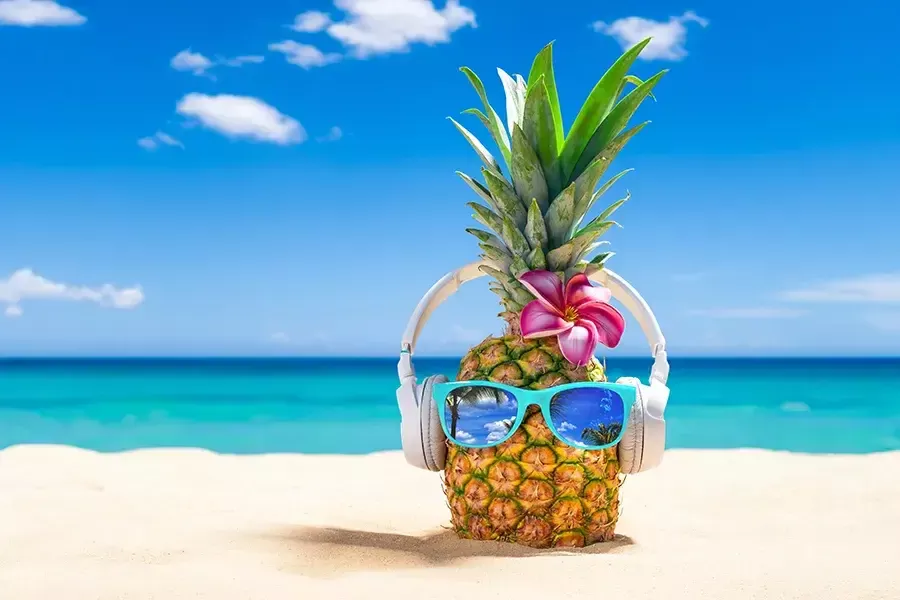 Tropical beach with a pineapple on it. The pineapple is wearing sunglasses and headphones