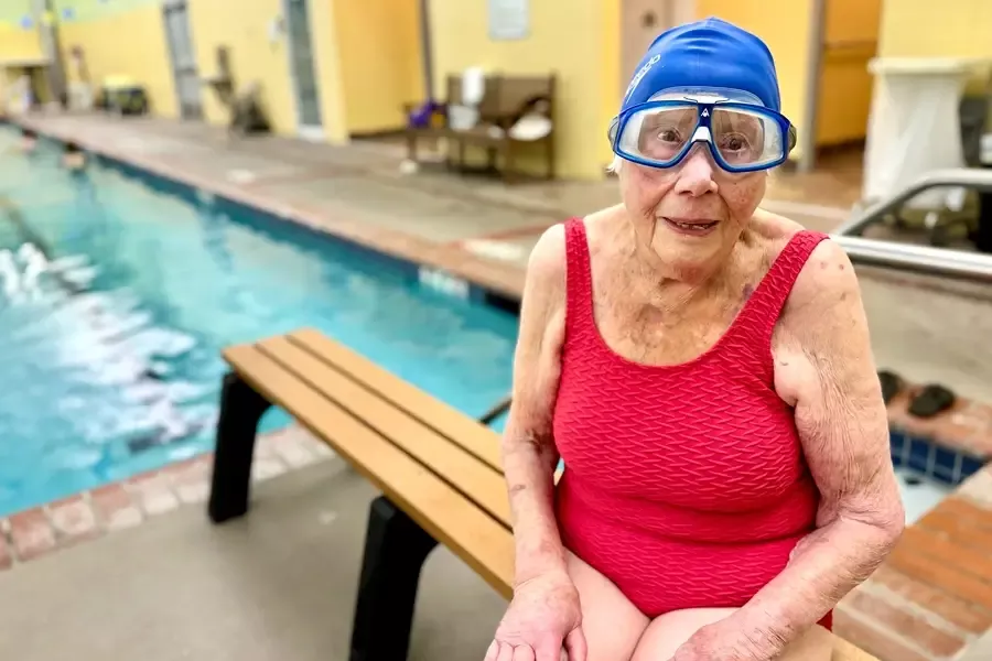 Regina Dembo sits beside pool in swimming cap and goggles